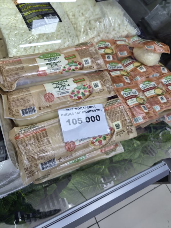 Витрина с сыром Bonfesto: моцарелла для пиццы в вакуумной упаковке 1 кг на ценнике «СЫР МОЦАРЕЛЛА ПИЦЦА 1КГ (BONFESTO)», рядом сулугуни Bonfesto, сверху тёртая моцарелла в пакетах и шарик свежей моцареллы