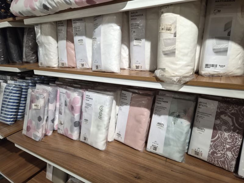 Полки с постельным бельём ARUA и IKEA-серий в упаковках: простыни на резинке «Натмина» White и NATTJASMIN, комплекты «пододеяльник и наволочки» ARUA «Натмина» Scandi, «Далия» Light pink, «Платмия» Royal, «Этель» Red; на упаковках наклейки с ценой