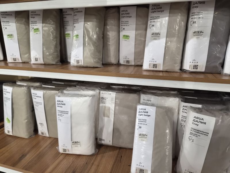 Полки с постельным бельём ARUA: простыни на резинке «Натмина» Beige, «Далия» Light beige и Grey 160×200, комплекты «пододеяльник и 2 наволочки» «Натмина» Beige, «Далия» White и Grey, ÄNGSLILJA, ULLVIDE; на упаковках наклейки с ценой, часть выделена зелёным маркером