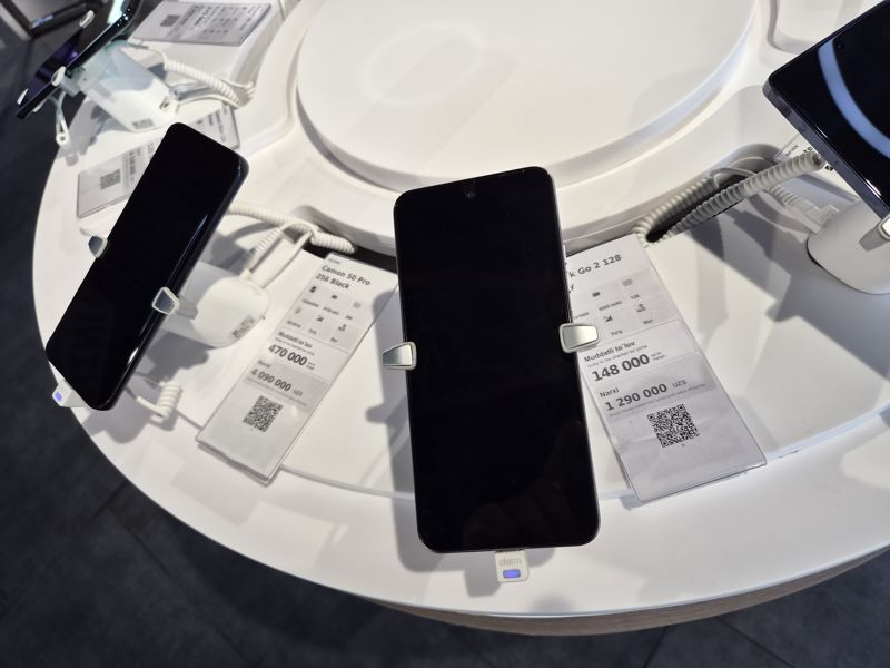 Круглая выставочная стойка со смартфонами на противокражных держателях в офисе Ucell: ценники Tecno Camon 50 Pro, Spark Go 2, Camon Slim