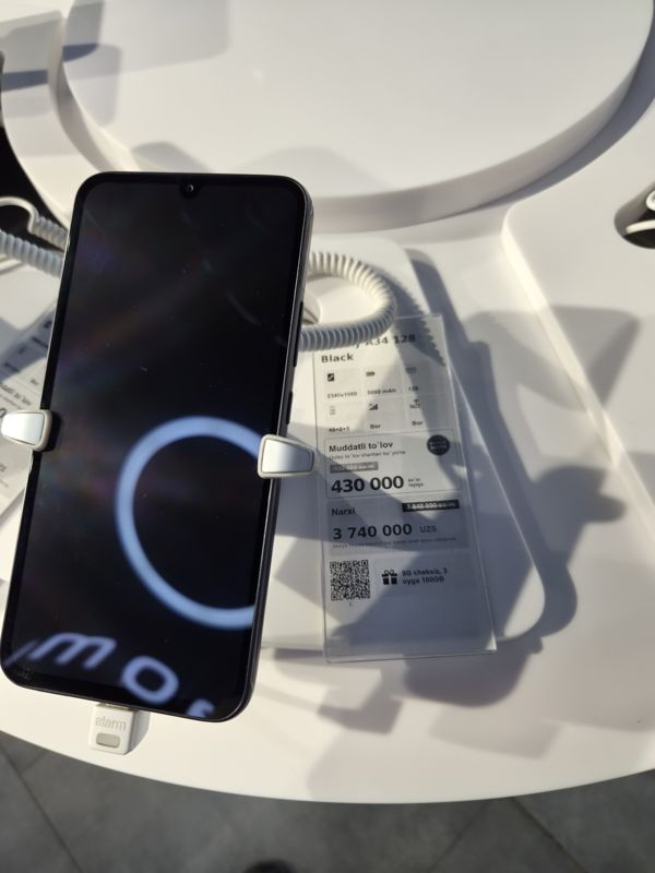 Смартфон Samsung Galaxy A34 на подставке с ценником Ucell: перечёркнутая прежняя цена, плашка «Maxsus aksiya» и подарок «5G cheksiz, 3 oyga 100GB»