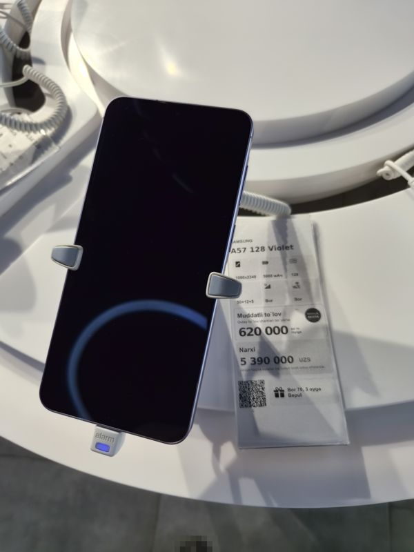 Смартфон Samsung A57 на подставке с ценником Ucell: плашка «Maxsus aksiya» и подарок «Bor 70, 3 oyga Bepul»