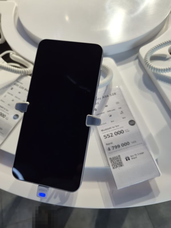 Смартфон Samsung Galaxy A56 на подставке с ценником Ucell: плашка «Maxsus aksiya» и подарок «Bor 70, 3 oyga Bepul»