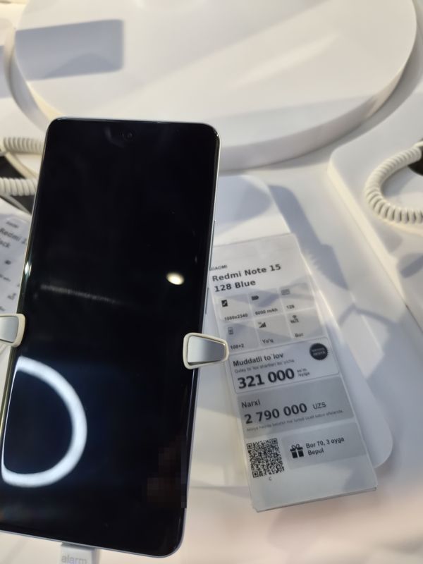 Смартфон Xiaomi Redmi Note 15 128 Blue на стенде Ucell, справа ценник-карточка с плашкой «Maxsus aksiya» и подарком к тарифу