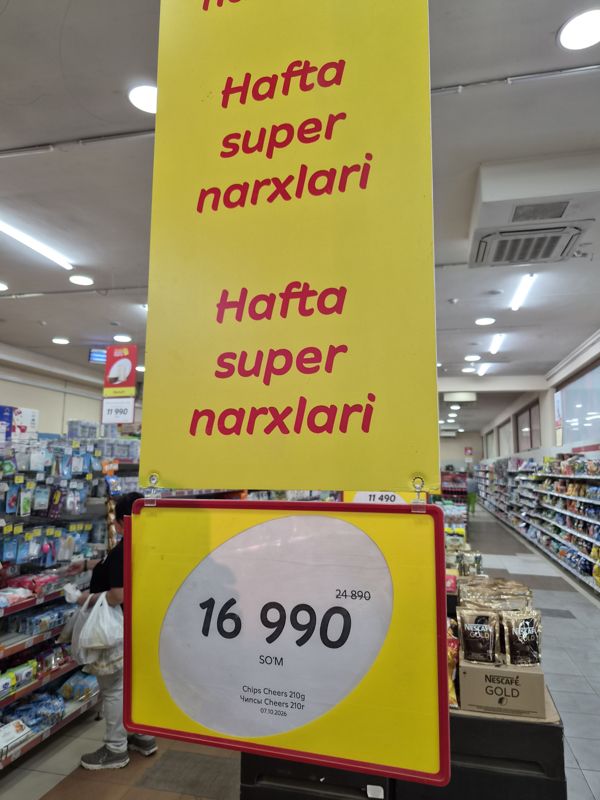 Подвесной постер «Hafta super narxlari» над горкой: ценник на чипсы Cheers 210 г