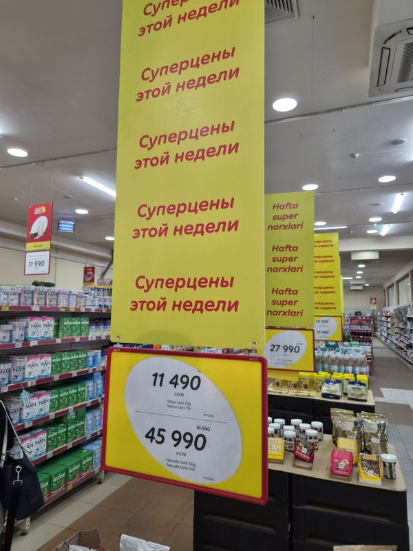 Подвесной постер «Суперцены этой недели» над горкой товаров: ценники на чипсы Lay's и Nescafe Gold