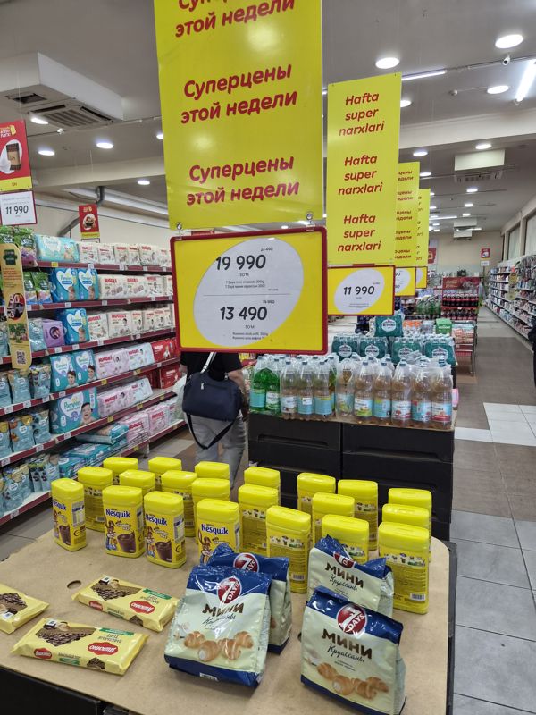 Горка с Nesquik, мини круассанами 7 Days и вафельными тортами Яшкино под постером «Суперцены этой недели», на заднем плане плакат «Yanada arzon narx!» с мукой