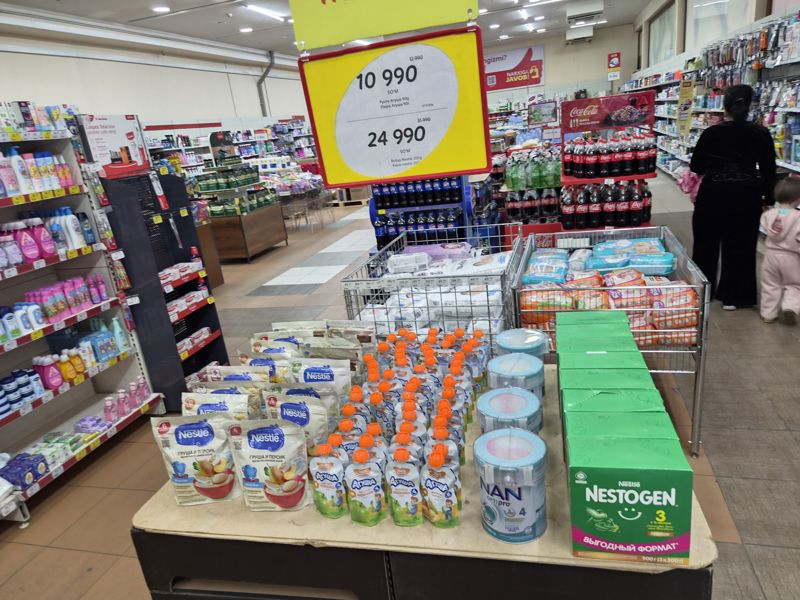 Стол с детским питанием Nestle, Агуша, NAN и Nestogen под подвесным ценником; слева детская косметика, справа стойка Coca-Cola и Pepsi