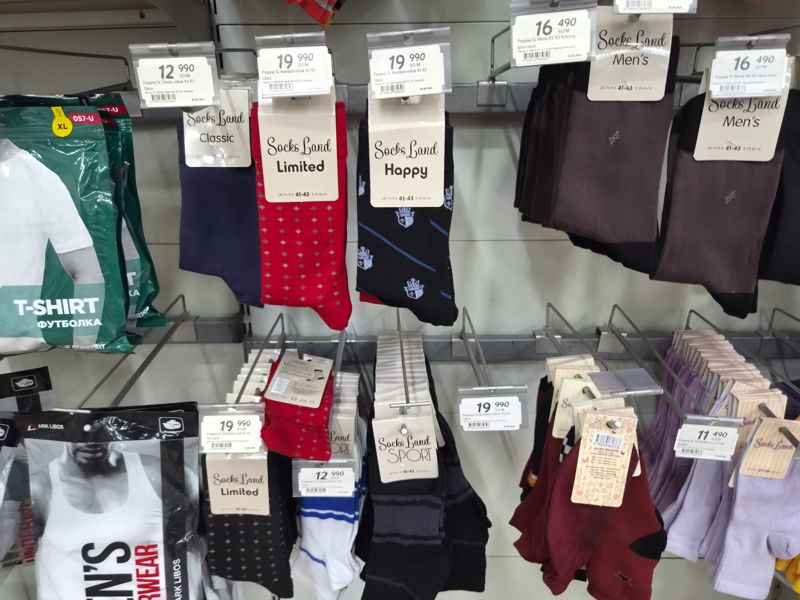 Мужские носки Socks Land (Classic, Bamboo, Limited, Happy, Mens, FlatSeams) на крючках, ценники на держателях; слева футболки