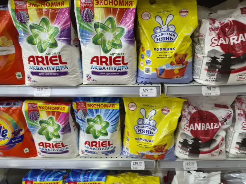 Полки со стиральными порошками Ariel Аква-Пудра, «Ушастый нянь», Sanraizu и Tide, ценники на кромках; кадр смазан