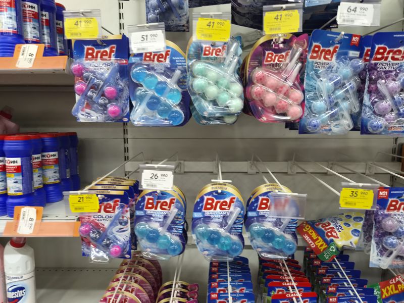 Подвесные туалетные блоки Bref (Color Aktiv Flower, BG Arctic Ocean, Deluxe Жасмин и Магнолия, Power Aktiv), ценники на крючках, жёлтые акционные; кадр смазан