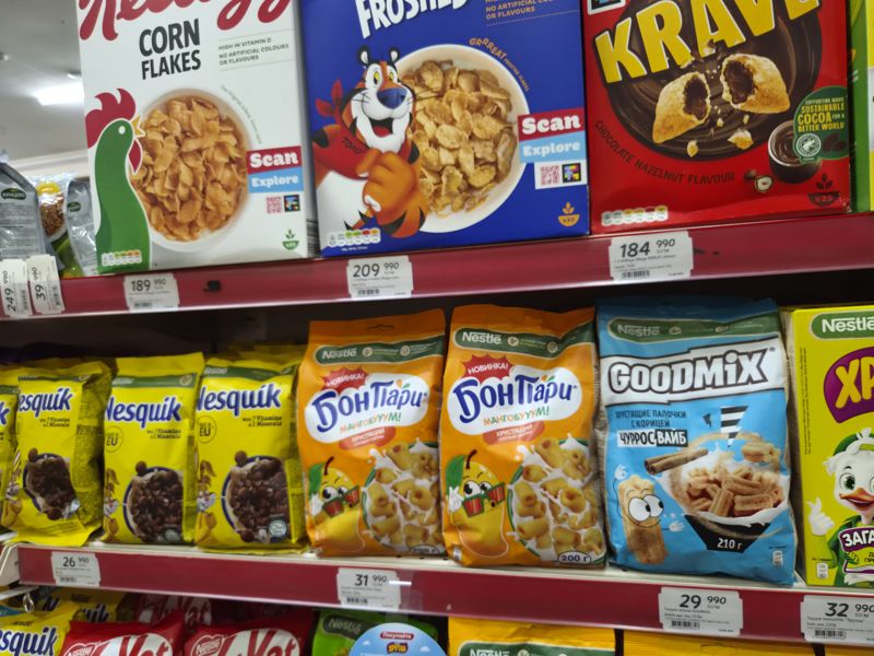 Стеллаж с готовыми завтраками: Kellogg's Corn Flakes, Frosties Mega и Krave (верхняя полка), Nesquik, «Бон Пари» манго, Goodmix «Чуррос Вайб», Хрутка (нижняя); белые полочные ценники под полками