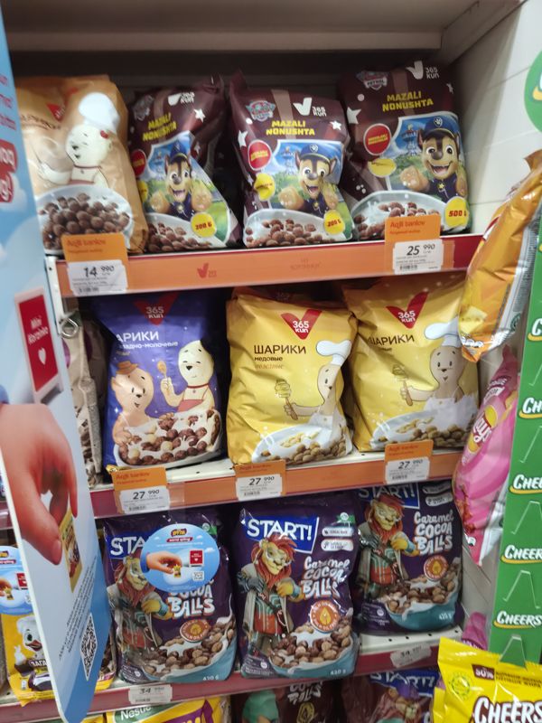 Стеллаж с готовыми завтраками собственной марки 365 kun (Paw Patrol «Mazali nonushta» 200 и 500 г, шарики молочные, медовые) и START! Caramel Cocoa Balls 420 г; на полках оранжевые плашки «Aqlli tanlov / Разумный выбор» над белыми ценниками