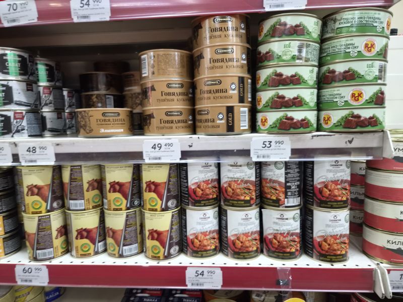 Полка и стеллаж с тушёнкой: Foodmaxx говядина тушёная кусковая (обычная, Gold, Элитная), консервы RGK, Halol, «Слободская» говядина; на полках белые ценники