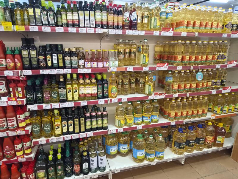 Стеллаж с оливковым маслом и уксусами: Basso, Olymp, ITLV, Borges, Kotanyi, Taris, Filippo Berio; ниже подсолнечное масло, слева кетчуп Picanto; ценники и плашки «Narxiga javob!»