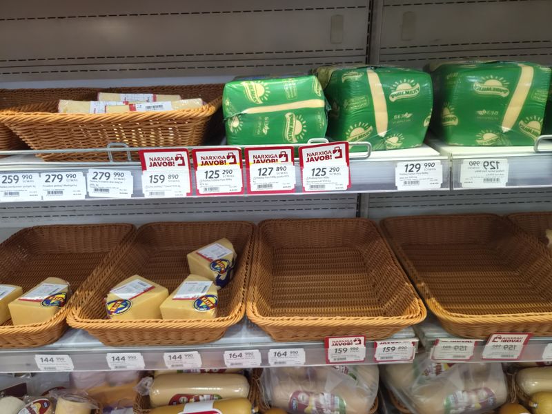 Сырная витрина: рулоны Pure Milky в зелёной упаковке над красными плашками «Narxiga javob!», корзины с сыром Kaser, ряды весовых ценников President, Pure Milky, Сваля; внизу Kaser, Щедрые Пружаны (SHP), «Алиса»