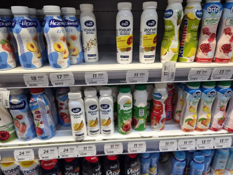 Холодильная витрина с питьевыми йогуртами: Нежный, Campina, Доброе, Kamilka, Lactel, Puremilky; на жёлтых наклейках «Uvol bo'lmasin -50%» на бутылках Доброе; ценники на кромках