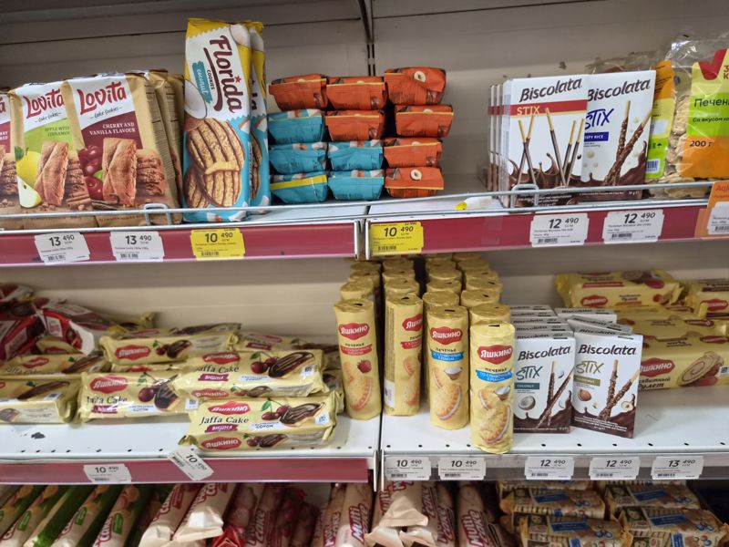 Стеллаж с печеньем: Lovita (яблоко-корица, вишня-ваниль), Florida (кокос, тёмное), Biscolata Stix, Яшкино (Jaffa Cake, с кремом, рулет); ценники на красных кромках, два жёлтых акционных «Hafta super narxlari»