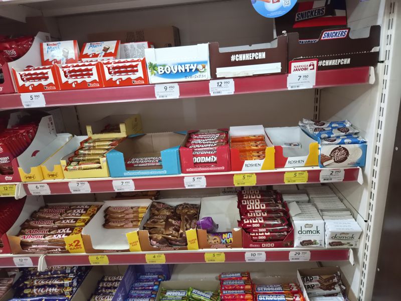 Полки с батончиками и шоколадом: Kinder Maxi, Bounty, Snickers, Goodmix, Roshen, BonTime, Albeni, Dido, Nestle Damak; жёлтые ценники «Hafta super narxlari»
