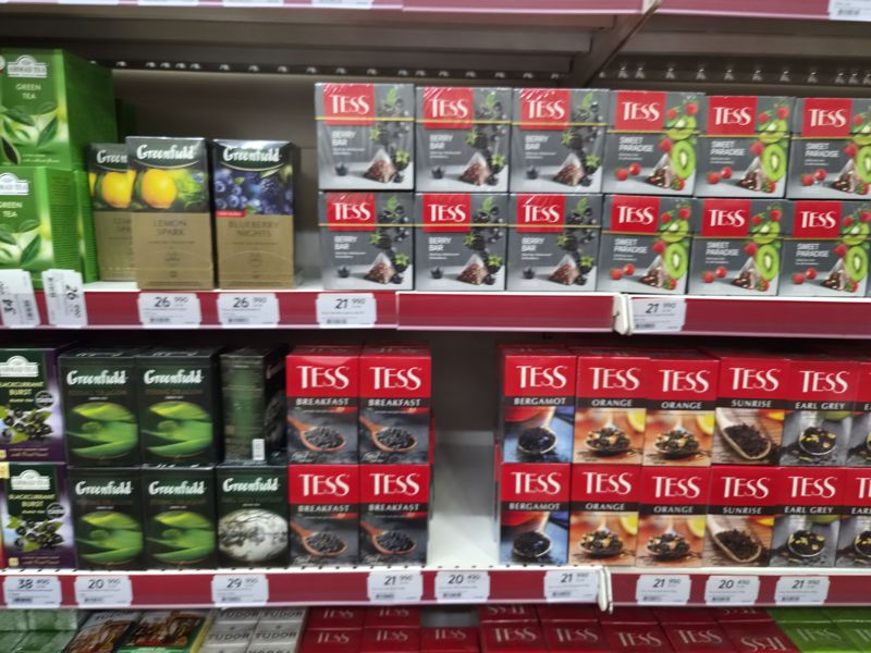Чай Greenfield (Lemon Spark, Blueberry Nights, Flying Dragon, Earl Grey Fantasy), Tess (Berry Bar, Sweet Paradise, Breakfast, Bergamot, Orange, Sunrise, Earl Grey) на полках; кадр снят с движением