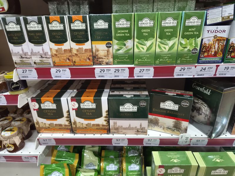 Полки с чаем Ahmad Tea (Earl Grey, Ceylon, English Tea No.1, Jasmine, Green, Mint, English Breakfast, большие пачки по 100 пакетиков), Tudor и Greenfield; чёткие ценники, один повёрнут вертикально