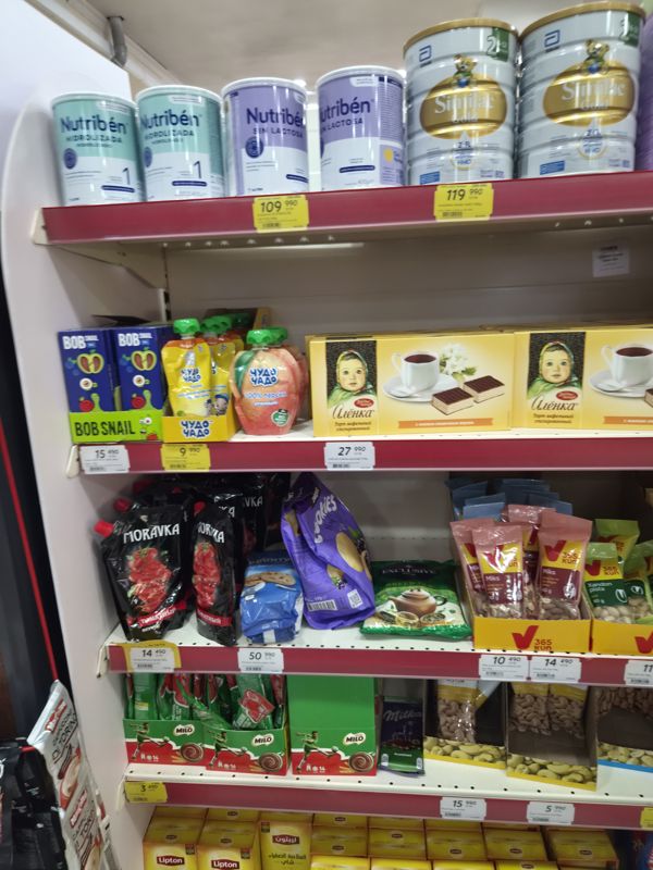 Стеллаж с детским питанием и сладостями: смеси Nutriben и Similac Gold, пюре Чудо-Чадо, Bob Snail, вафельный торт «Аленка», Moravka, печенье Bounty, орехи 365 kun, какао Milo, Milka, чай Lipton; жёлтые и белые ценники