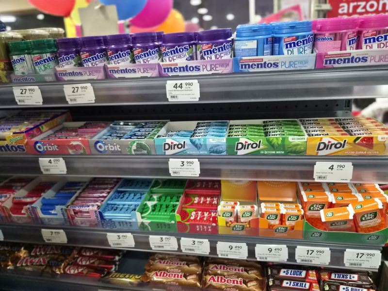 Стеллаж с жевательной резинкой и драже: Mentos Pure Fresh, Orbit, Dirol, STYX, Tic Tac; внизу шоколадные батончики; ценники с штрихкодами на полках