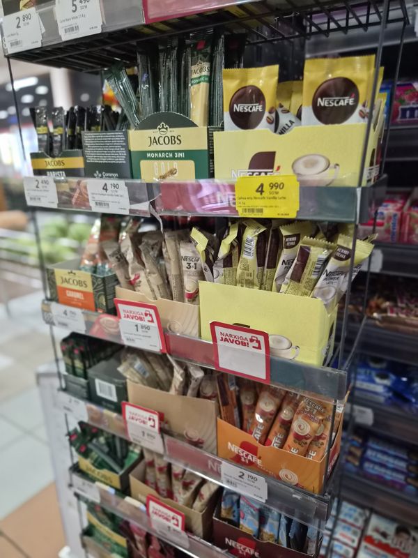 Угловая стойка со стиками кофе 3 в 1: Jacobs, Nescafe (Classic, Mild, Caramel, Ice, Plombir Latte, Vanilla Latte), Carte Noire; жёлтый ценник и ценники «Narxiga javob!»