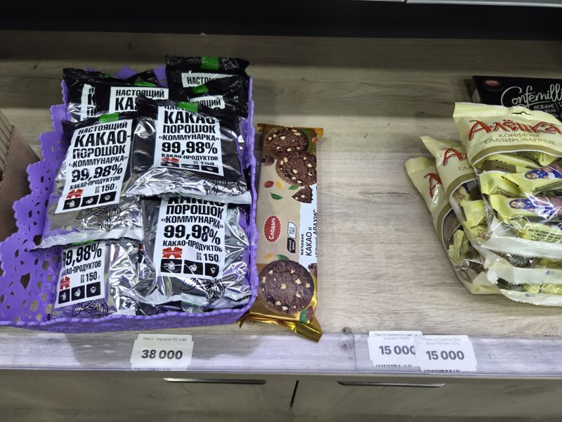 Полка с какао-порошком «Коммунарка» в корзине, печенье Слодыч с какао и арахисом и конфеты «Аленка», внизу ценники