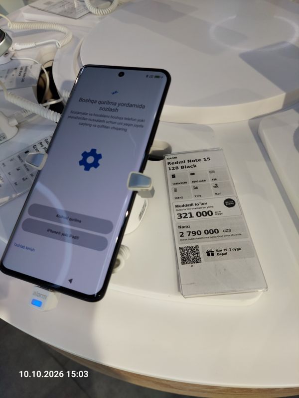 Смартфон Xiaomi на витрине Ucell в держателе с сигнализацией, на экране экран настройки, рядом ценник-карточка: XIAOMI Redmi Note 15 128 Black, 2 790 000 сум