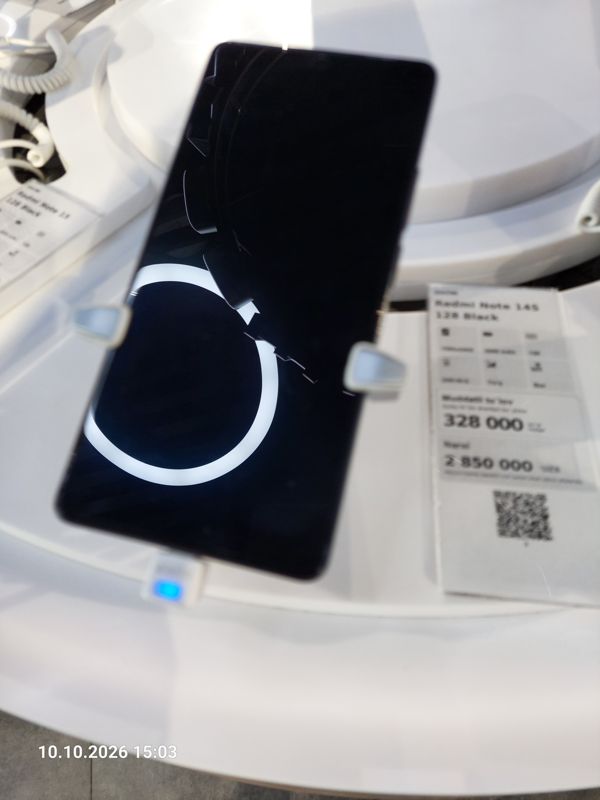 Смартфон Xiaomi на витрине Ucell в держателе с сигнализацией, рядом ценник-карточка «Redmi Note 14S 128 Black», кадр смазан движением