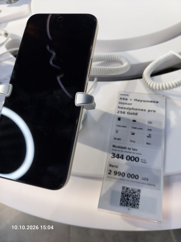 Смартфон Honor X6e в держателе на витрине Ucell, рядом ценник-комплект: HONOR X6e + наушники Honor headphones pro 256 Gold, 2 990 000 сум