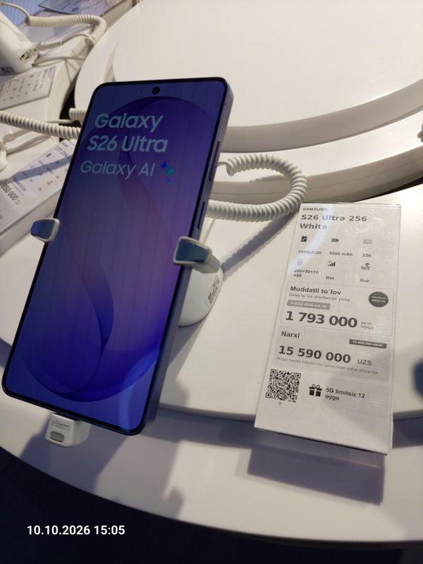 Смартфон Samsung Galaxy S26 Ultra в держателе с сигнализацией на витрине Ucell, рядом ценник-карточка: SAMSUNG S26 Ultra 256 White, плашка «Maxsus aksiya», 15 590 000 сум, перечёркнутая прежняя цена 15 890 000
