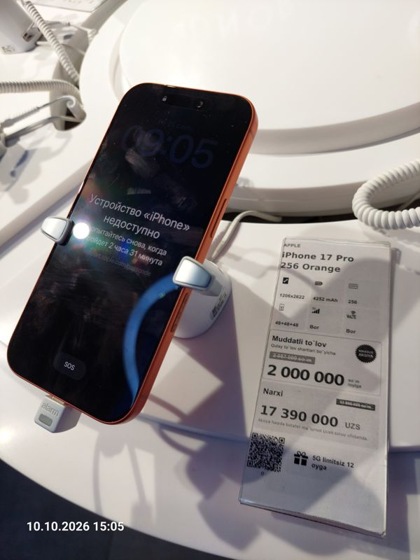 Смартфон iPhone 17 Pro (оранжевый) в держателе с сигнализацией на витрине Ucell, рядом ценник-карточка: APPLE iPhone 17 Pro 256 Orange, плашка «Maxsus aksiya», 17 390 000 сум, перечёркнутая прежняя цена 17 890 000