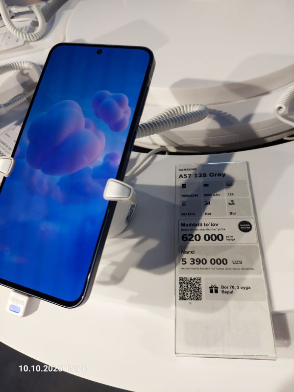 Смартфон Samsung A57 в держателе с сигнализацией на витрине Ucell, рядом ценник-карточка: SAMSUNG A57 128 Gray, плашка «Maxsus aksiya» и подарок «Bor 70, 3 oyga Bepul», 5 390 000 сум