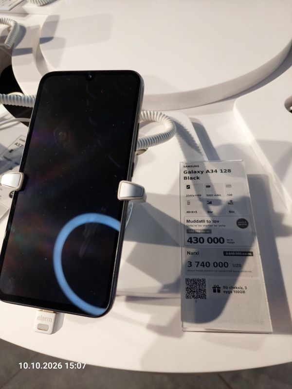 Смартфон Samsung Galaxy A34 на подставке с ценником Ucell: перечёркнутая прежняя цена, плашка «Maxsus aksiya» и подарок «5G cheksiz, 3 oyga 100GB»