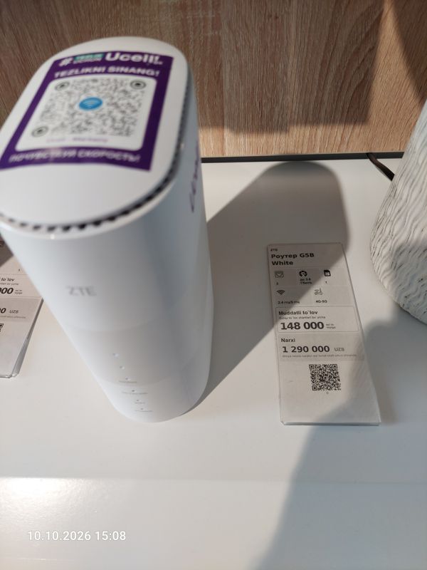 5G-роутер ZTE с наклейкой Ucell «Tezlikni sinang!» (QR для подключения к Wi-Fi) на столе, справа ценник-карточка: Роутер G5B White, 1 290 000 сум