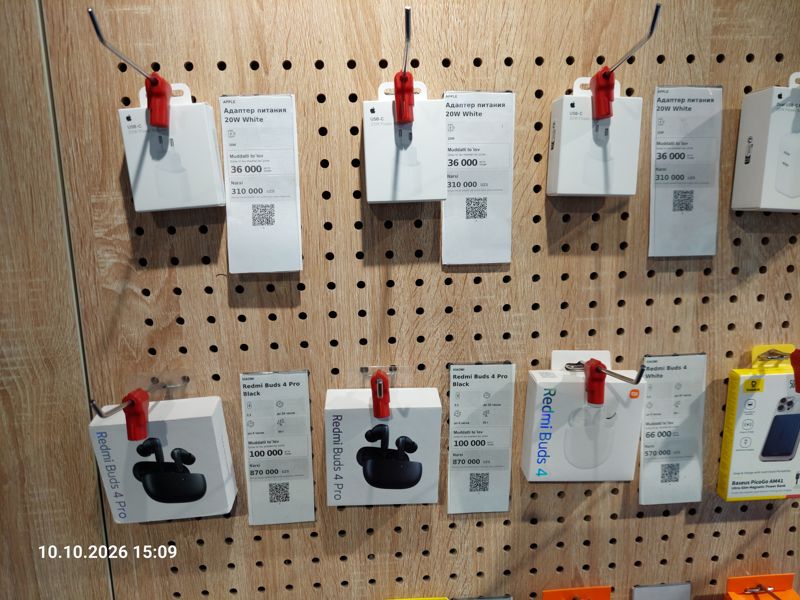 Стенд аксессуаров на перфорированной панели в офисе Ucell: адаптеры питания Apple 20W, наушники Redmi Buds 4 Pro и Buds 4 с ценниками-карточками
