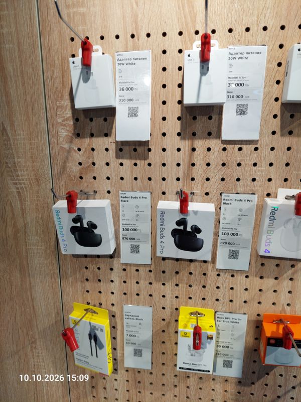 Левая часть стенда аксессуаров в офисе Ucell: адаптеры питания Apple 20W, наушники Redmi Buds 4 Pro, кабель и наушники Baseus с ценниками-карточками