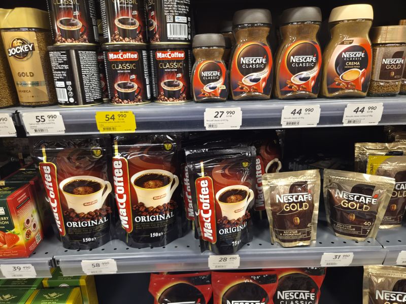 Полки с растворимым кофе: Jockey, MacCoffee, Nescafe Classic и Gold, Jacobs; ценники на кромках полок, один жёлтый со старой ценой