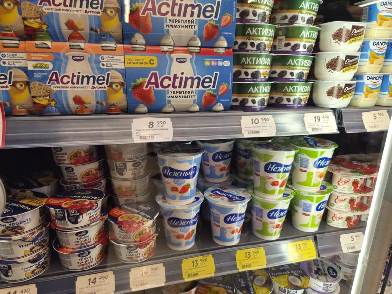 Холодильная витрина с йогуртами: Actimel и Activia сверху, творожный Danissimo и Danone, ниже «Нежный», греческий йогурт «Доброе», Engil; ценники на кромках, три жёлтых акционных у «Нежного»