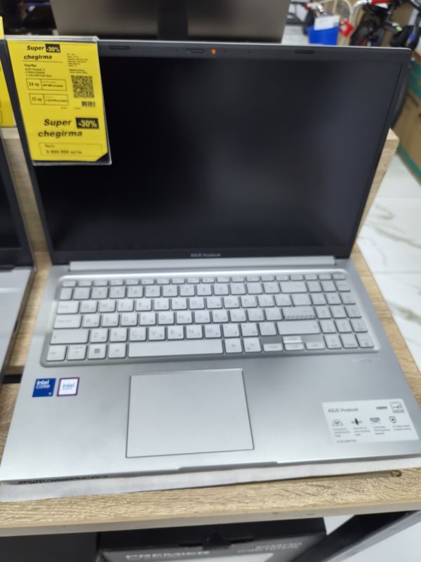 Ноутбук ASUS Vivobook 15 серебристого цвета на деревянной полке с жёлтым ценником «Super chegirma -30%»