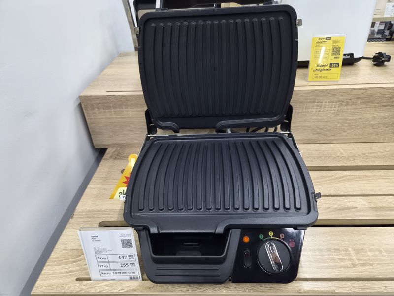 Гриль Tefal GC450B32 с открытыми греющими панелями на деревянной полке, перед ним белый ценник; справа в глубине белый тостер Braun с жёлтым ценником «Super chegirma -20%»