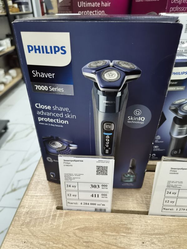 Электробритва Philips Shaver 7000 Series в коробке с белым ценником и рядом коробка Philips 5000X на полке магазина электроники