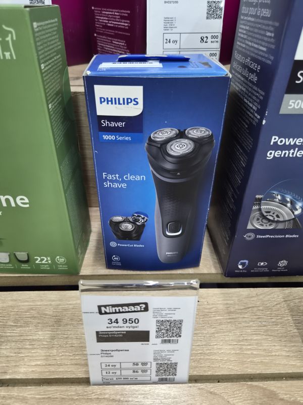 Электробритва Philips Shaver 1000 Series в синей коробке на полке магазина электроники, под ней белый ценник магазина