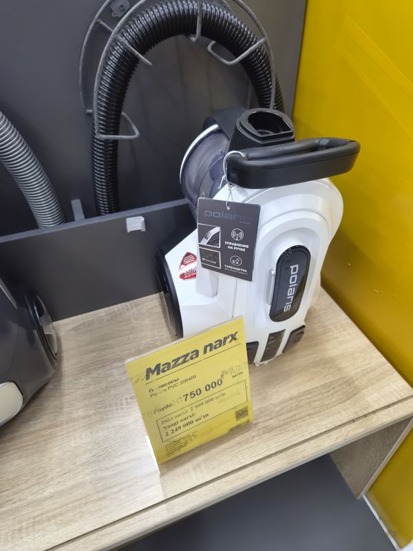 Пылесос Polaris PVC 2004RI с контейнером на полке стенда, перед ним жёлтый акционный ценник «Mazza narx»