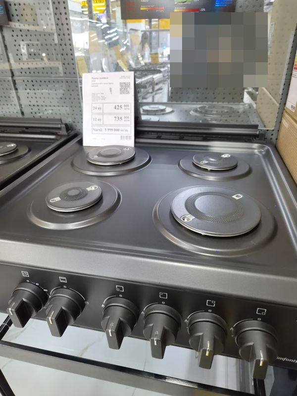 Газовая плита Artel Simfoniya с четырьмя газовыми конфорками и духовкой, чёрная матовая, на витрине зала; перед ней белый ценник «Плиты газовые»