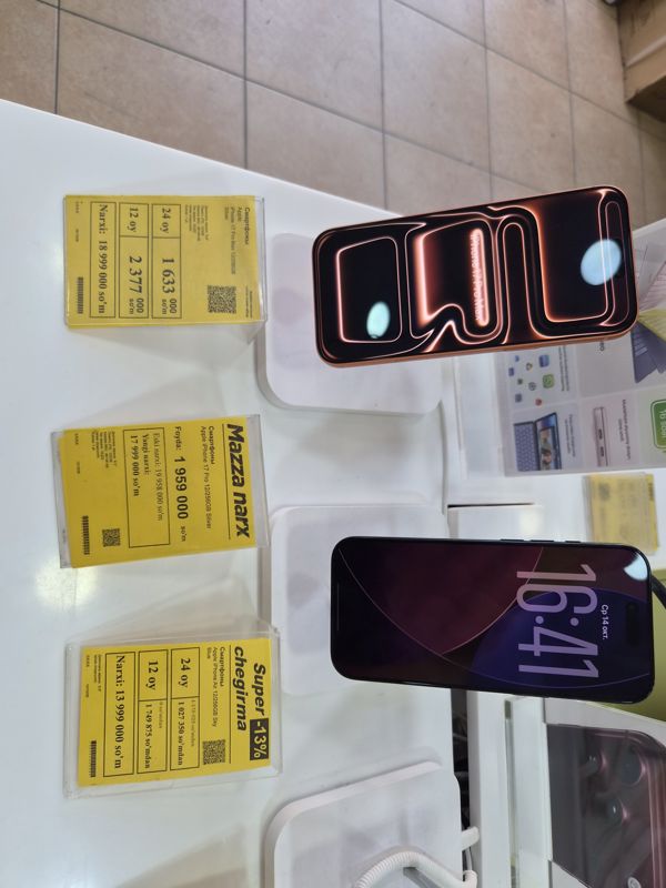 Три жёлтых ценника Техномарта на витрине смартфонов Apple: iPhone 17 Pro Max, iPhone 17 Pro («Mazza narx») и iPhone Air («Super chegirma -13%»), рядом два смартфона на подставках