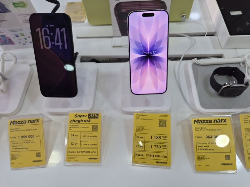 Четыре жёлтых ценника Техномарта на витрине iPhone: 17 Pro («Mazza narx»), Air («Super chegirma -13%»), 17 и 17e («Mazza narx»); над ними два смартфона на подставках и умные часы