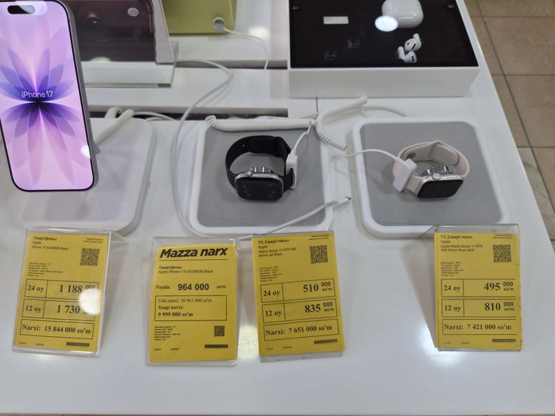 Два смартфона на подставках и на столе ценники Техномарта: iPhone 17 (8/256GB), iPhone 17e («Mazza narx») и два ценника умных часов Apple Watch Series 11